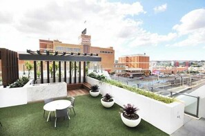 Une terrasse sur le toit, avec une table et des chaises, des plantes en pot et une vue sur le paysage urbain.