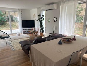 A modern living room with a dining area, large windows, and a flat-screen TV. - House between the city and the countryside near Lyon (Saint-Genis-Laval)