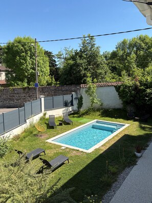 A rectangular swimming pool with a tiled edge, surrounded by a grassy area with lounge chairs and a stone wall. - House between the city and the countryside near Lyon (Saint-Genis-Laval)