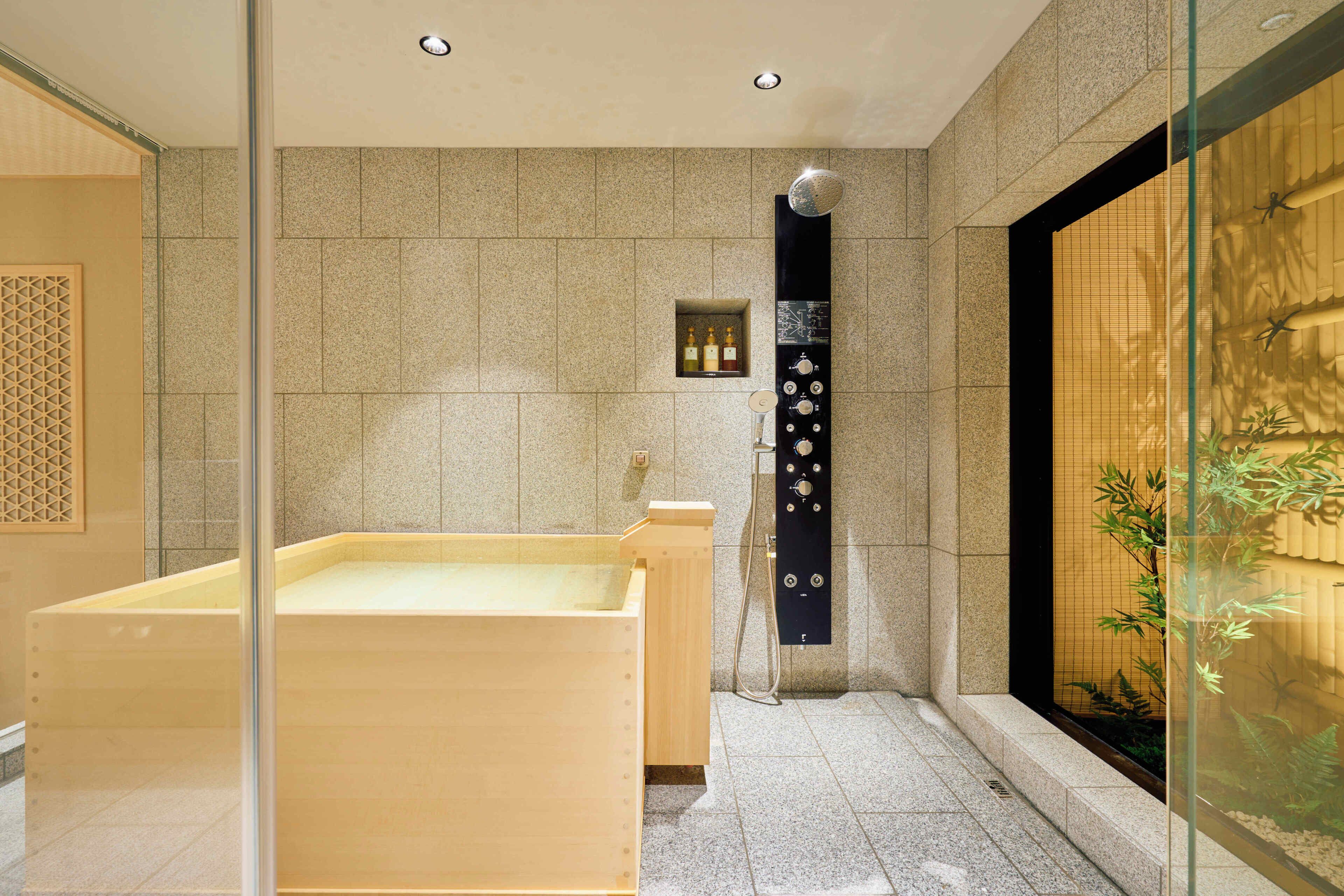 Un baño moderno con una bañera de madera, una cabina de ducha de vidrio y una planta de bambú.