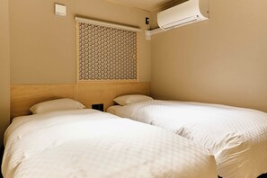 Ein Hotelzimmer mit zwei Betten, einem Holzkopfstück, einer Klimaanlage und einem Fenster mit einem gemusterten Rollo.