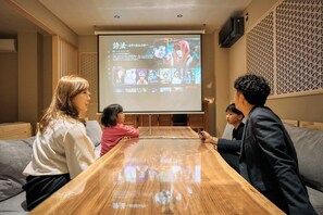 Eine Gruppe von Personen sitzt an einem Holztisch in einem Raum, in dem ein Projektionsschirm eine Netflix-Oberfläche zeigt.