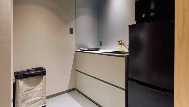 A compact kitchen with a black refrigerator, a small countertop, and a trash bin. - Imakusa-so, Osaka: Tempozan - Ikisu - (大阪府大阪市港区築港3丁目10−11)