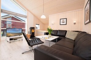 Ein modernes Wohnzimmer mit großem Fernseher, Ledersofa, weißem Couchtisch und einer Topfpflanze.