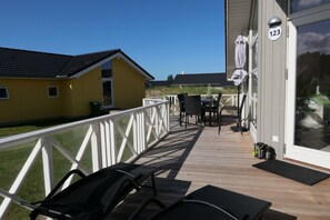 Eine Terrasse mit Gartenmöbeln, einem weißen Geländer und einem Gebäude mit Hinweisschild.