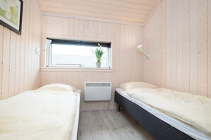 Ein kleiner Raum mit zwei Betten, einem Fenster mit Pflanze, einem Heizkörper und einer Wandleuchte.