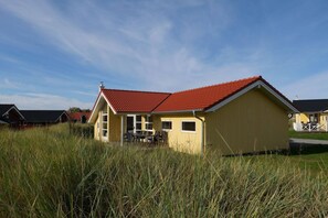 Un bâtiment jaune avec un toit rouge, entouré d’herbes hautes.