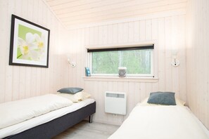 Ein Zimmer mit zwei Betten, einem Fenster mit Blick auf Grünflächen, einem Heizkörper und einem gerahmten Bild an der Wand.