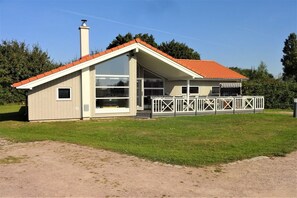 Una casa d'una sola planta amb teulada inclinada, grans finestres i un porxo cobert amb barana.