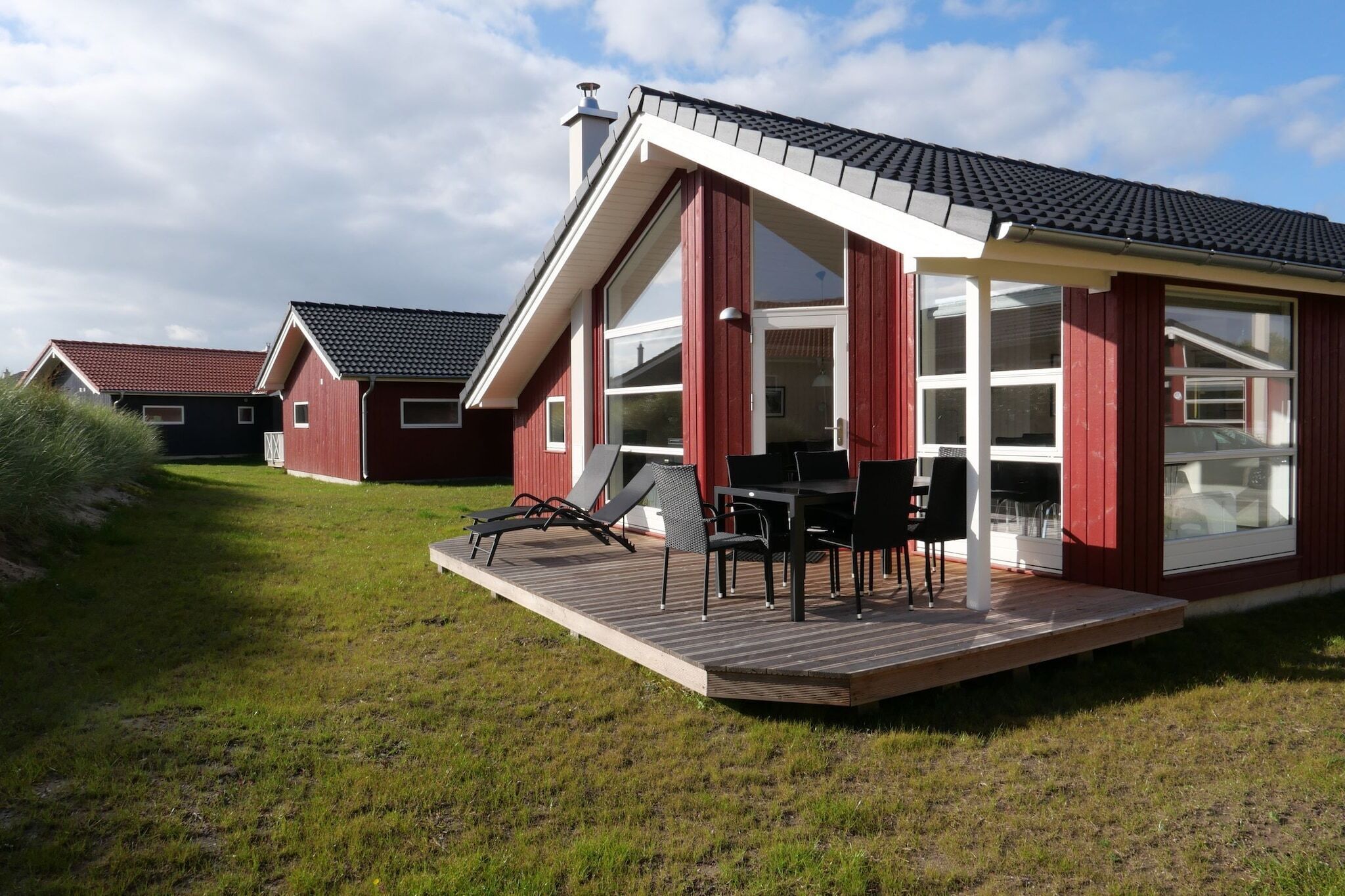Ein modernes Haus mit einer Terrasse, großen Fenstern und einer roten Fassade.