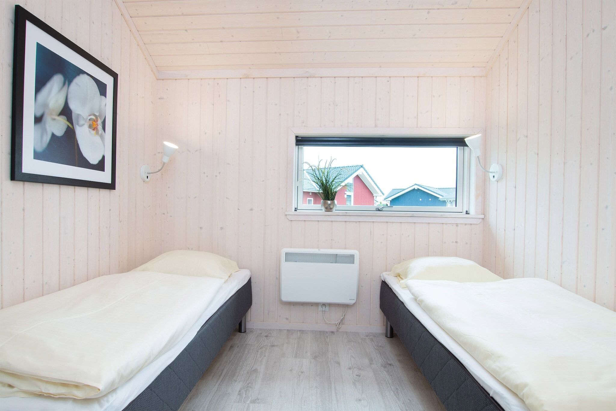 Ein Zimmer mit zwei Betten, einem Fenster mit Blick auf Häuser, einem Heizkörper und einer Wandleuchte.