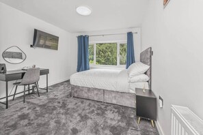 Une chambre à coucher avec un lit, un bureau, une chaise, un miroir et une fenêtre avec des rideaux.