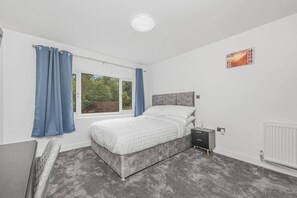 Ein Schlafzimmer mit einem Bett, einem Nachttisch, einem Heizkörper und einem Fenster mit Vorhängen.
