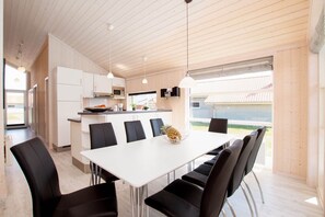 A modern kitchen with white cabinets, a dining table with chairs, and a large window. - Charming Cottage for 8 with Sauna (Großenbrode)