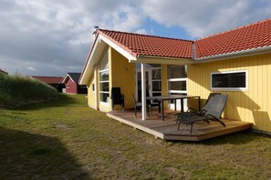 Ein gelbes Gebäude mit rotem Ziegeldach, einer Holzterrasse und einem Tisch mit Stühlen.