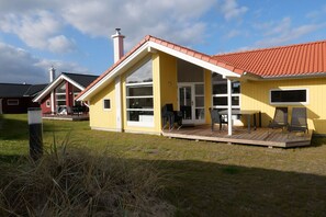 Een geel gebouw met een rood dak, grote ramen en een overdekt terras met buitenmeubilair.
