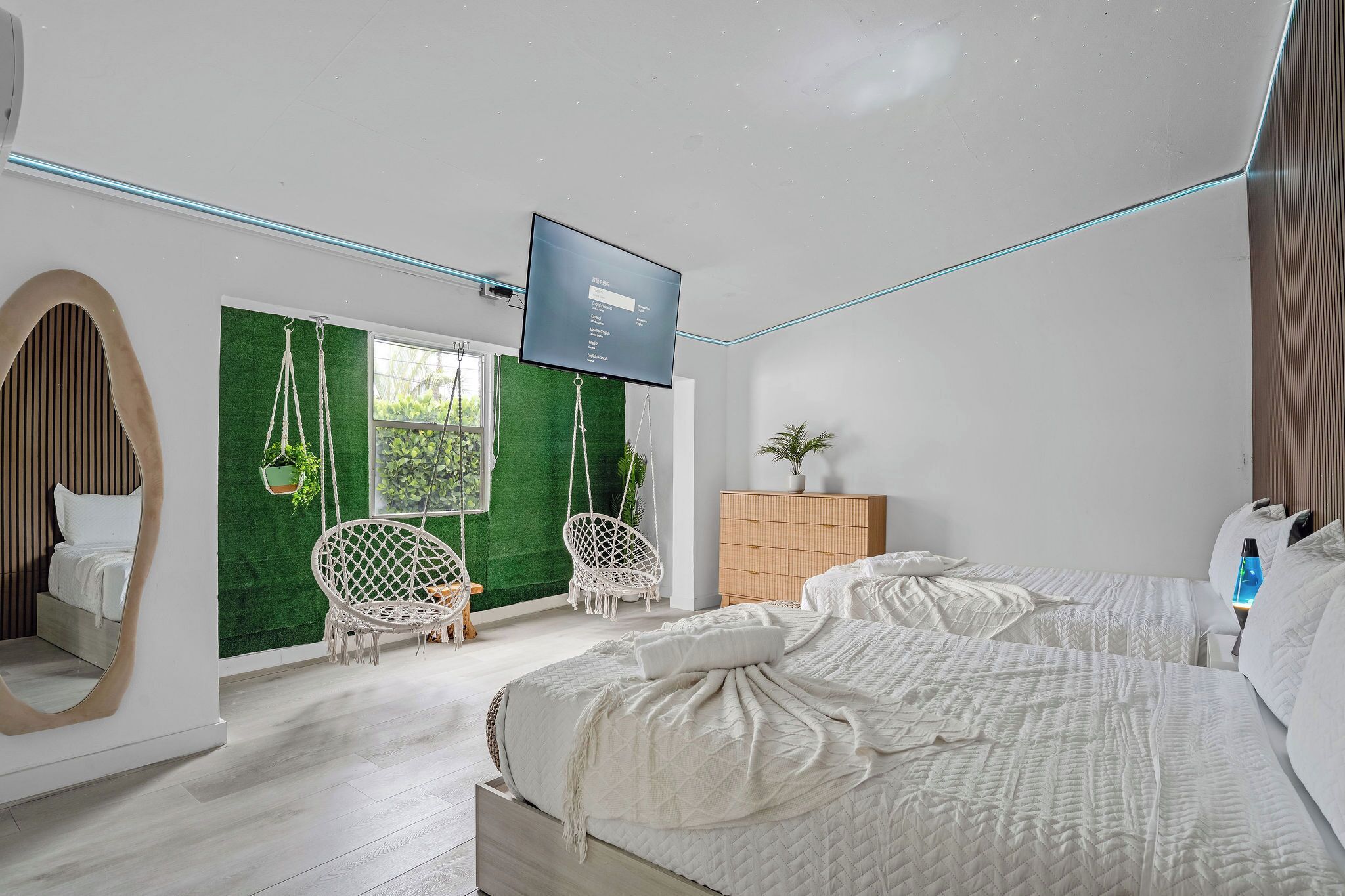 Quarto moderno com cama, duas cadeiras penduradas, uma TV e um armário de madeira.