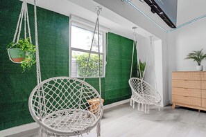 Ein Zimmer mit zwei Hängestühlen aus Makramee, einer Holzschrank und einem Fenster mit Blick ins Grüne.