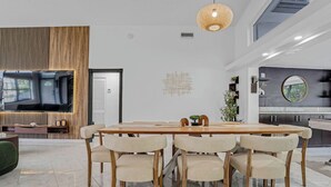 A modern dining area with a wooden table and chairs, a television, and a decorative wall piece. - Waterfront House with Tiki & Firepit (Miami)