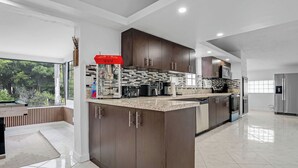 A modern kitchen with dark cabinetry, a marble countertop, and stainless steel appliances. - Waterfront House with Tiki & Firepit (Miami)