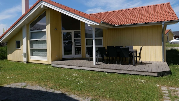A single-story house with a red-tiled roof, a covered patio with outdoor furniture, and a chimney. - Kustenparadies fur 8 Gaste (Grossenbrode)