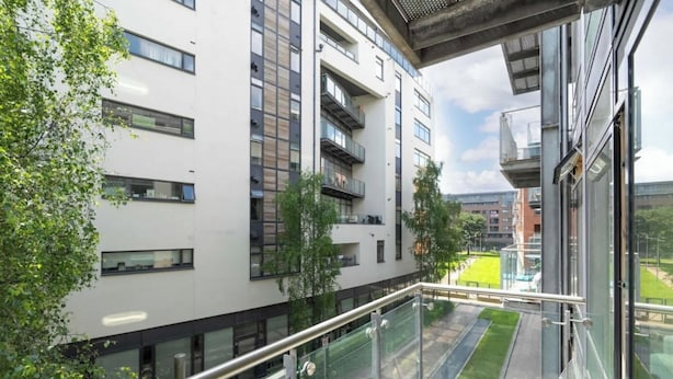 Ein modernes Gebäude mit mehreren Etagen, großen Fenstern und einem Balkon mit Glasgeländer.