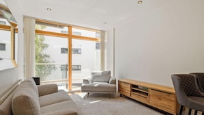Ein modernes Wohnzimmer mit einer Couch, einem Sessel, einer Holz-Unterhaltungseinheit und einem großen Fenster mit Blick nach draußen.