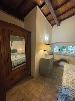 A bedroom with a wooden wardrobe, a bedside table with a lamp, a radiator, and a window with a view of trees. - The Casalino Orvieto Dépendance. A hidden oasis surrounded by greenery, 15 minutes from Orvieto (Umbria)