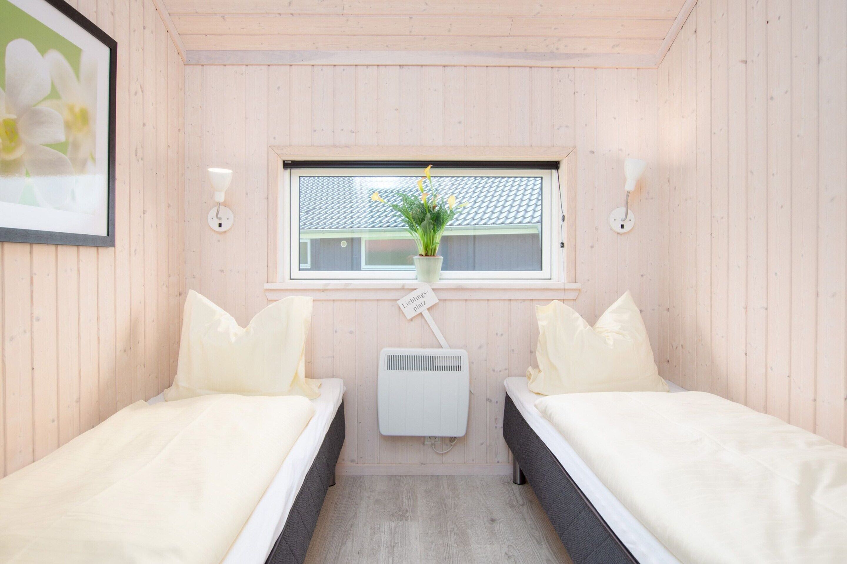 A room with two beds, a window with a view of a building, a wall-mounted air conditioner, and a framed picture on the wall.