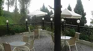 An outdoor patio with round tables and chairs, surrounded by a gravel area and a black metal railing.