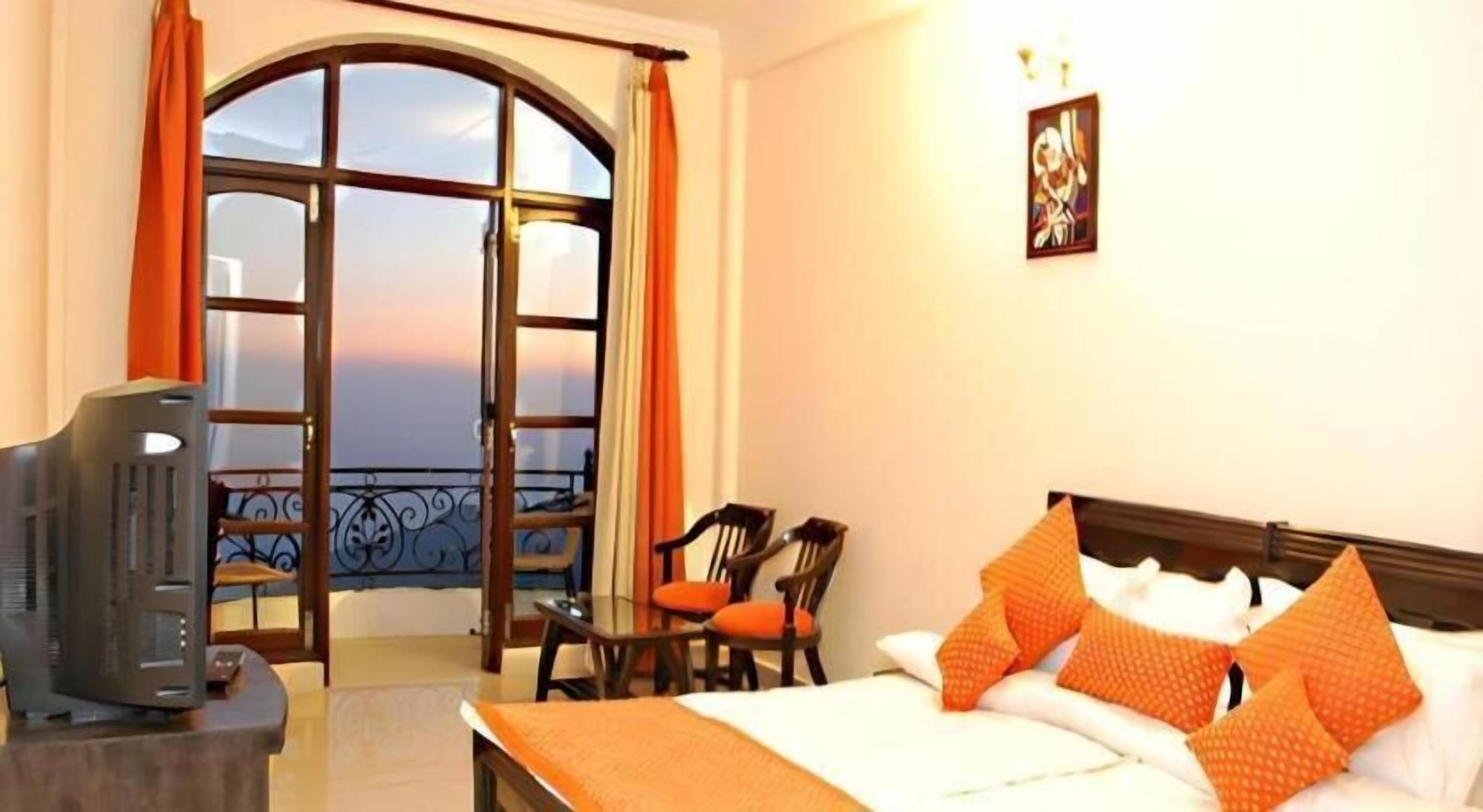 A hotel room with a bed, a television, a balcony with a view, and a table with chairs.