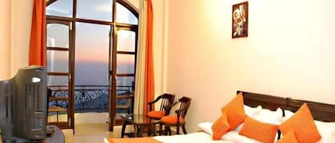 A hotel room with a bed, a television, a balcony with a view, and a table with chairs.