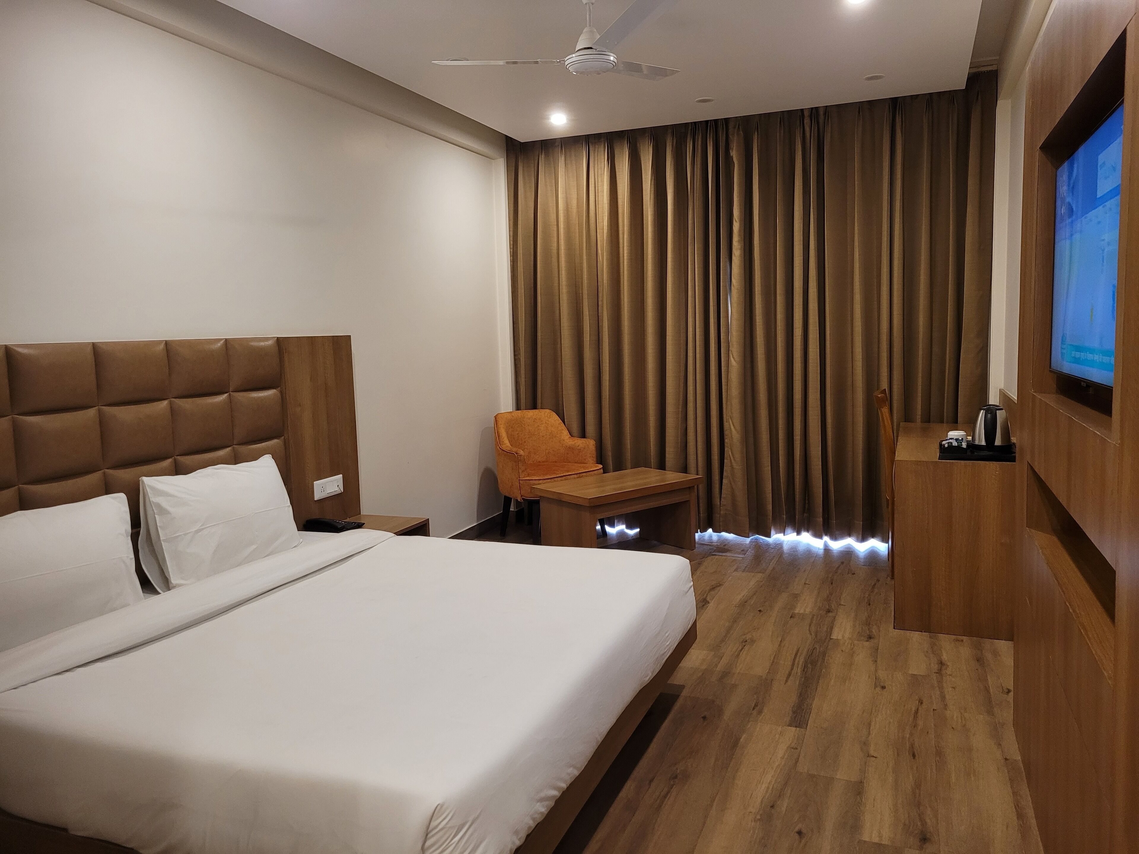 Una habitación de hotel con una cama grande, un escritorio, una silla, un televisor y un ventilador de techo.