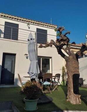 A residential property with a well-maintained lawn, a large tree, outdoor furniture, and a building with a tiled roof.