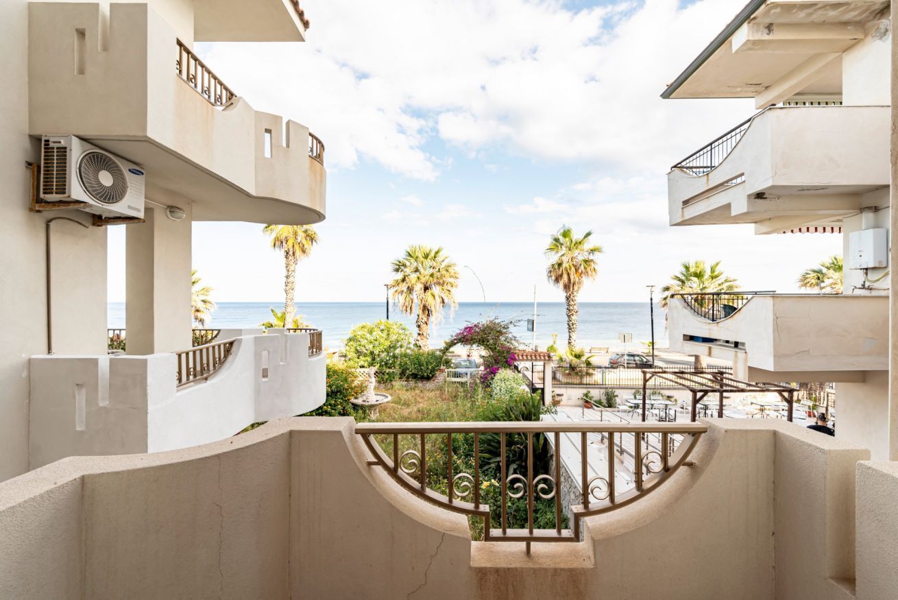 Un balcon avec vue sur la mer, des palmiers et un jardin.