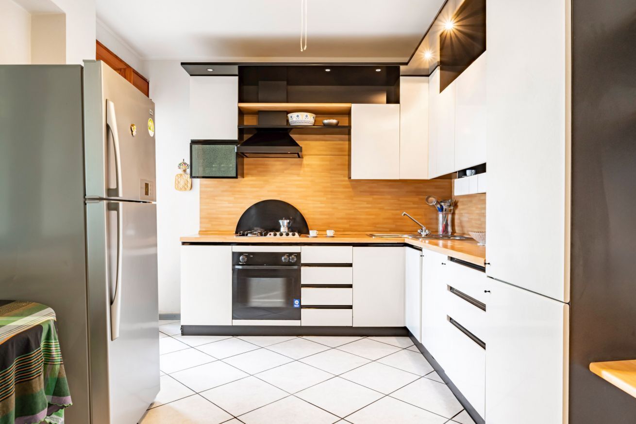 Een moderne keuken met witte kasten, een ingebouwde oven en een koelkast van roestvrij staal.
