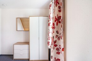 Un dormitorio con armario, espejo y cama con cortina estampada.