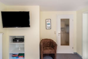 A living room with a flat-screen TV, a framed photo, a brown armchair, and a door with a frosted glass panel. - Apartment 'Kuhlmann' with Mountain View and Wi-Fi (Landkreis Goslar)