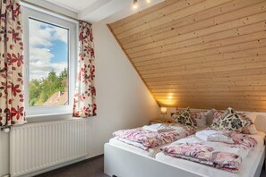 A bedroom with a sloped ceiling, a bed with floral bedding, a window with curtains, and a radiator. - Apartment 'Kuhlmann' with Mountain View and Wi-Fi (Landkreis Goslar)