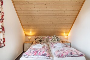Un dormitorio pequeño y acogedor con dos camas individuales, techo de madera y lámparas de noche.