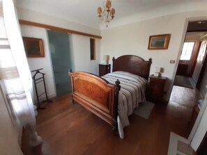 Ein Schlafzimmer mit einem hölzernen Bett, einem Nachttisch, einer Lampe und einer Tür zu einem anderen Raum.