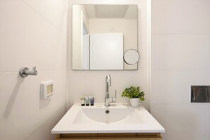 A bathroom with a white sink, a mirror, a faucet, a potted plant, and toiletries on the counter. - Bright Spacious Stay with Balcony (Tel Aviv)