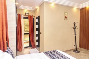 Habitación de hotel con cama, perchero y puerta que da a un balcón.