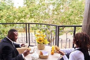 A man and a woman sitting at an outdoor table with a view of trees, a metal railing, and a basket of sunflowers.