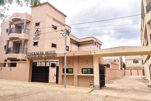 Un hotel con fachada color beige, varios balcones y una entrada protegida por una reja.