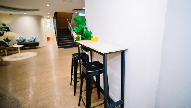 Un interior moderno con piso de madera, una mesa blanca con taburetes negros y una escalera que sube a un nivel superior.