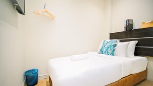 Habitación de hotel con cama, cabecero de madera, un cesto de basura azul y un perchero de madera en la pared.