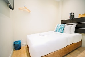 Habitació d'hotel amb un llit, un panell de capçalera de fusta, un cisteller blau i una safata penjada a la paret.