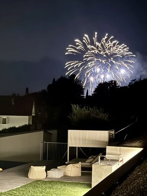 A modern outdoor seating area with a firework display in the background. - Villa Aqua by Elite Villas (Tremezzina)
