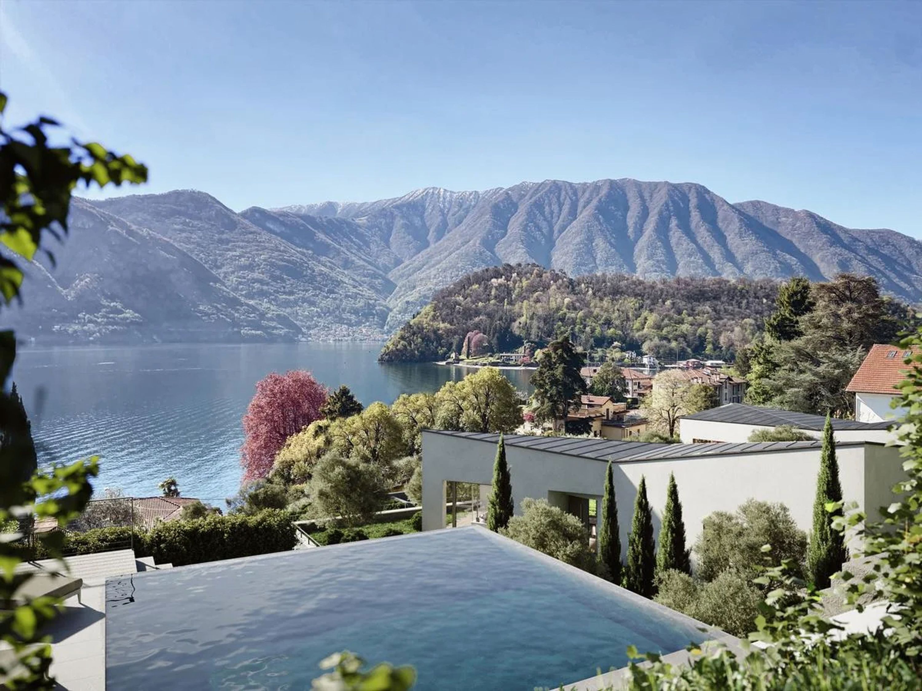 A modern building with a rooftop pool overlooking a lake and mountains.